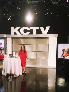 A woman avoiding beauty disasters stands in front of a television set wearing a red dress.