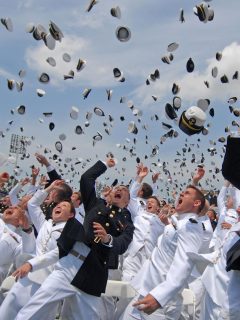 A group of Navy men in uniform tossing hats into the air.