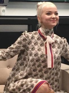 A woman, Dove Cameron, sitting on a chair with her arms outstretched during a Descendants 2 interview.