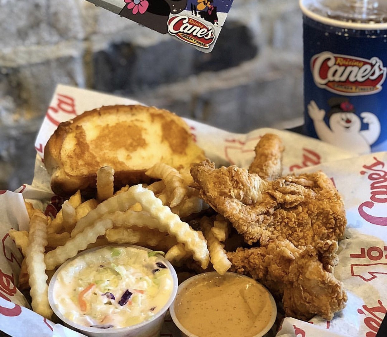 A basket of Raising Cane's fried chicken, french fries and a soda.