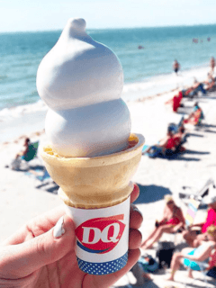 A person holding a cone of ice cream on the beach while enjoying their Dairy Queen treat.