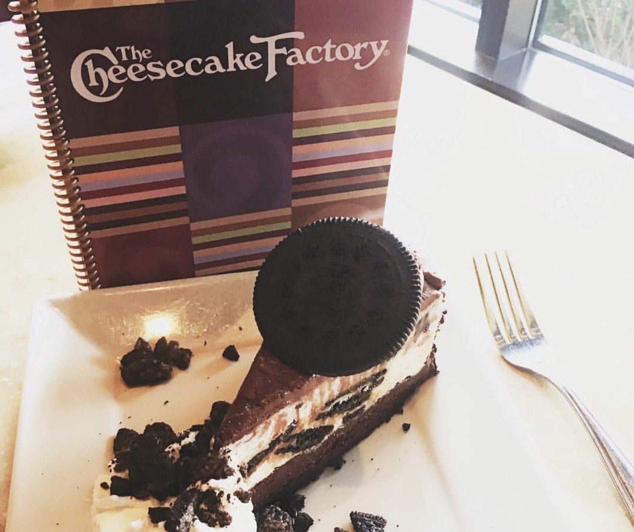 A decadent cheesecake dessert topped with an indulgent Oreo cookie, served on a plate.