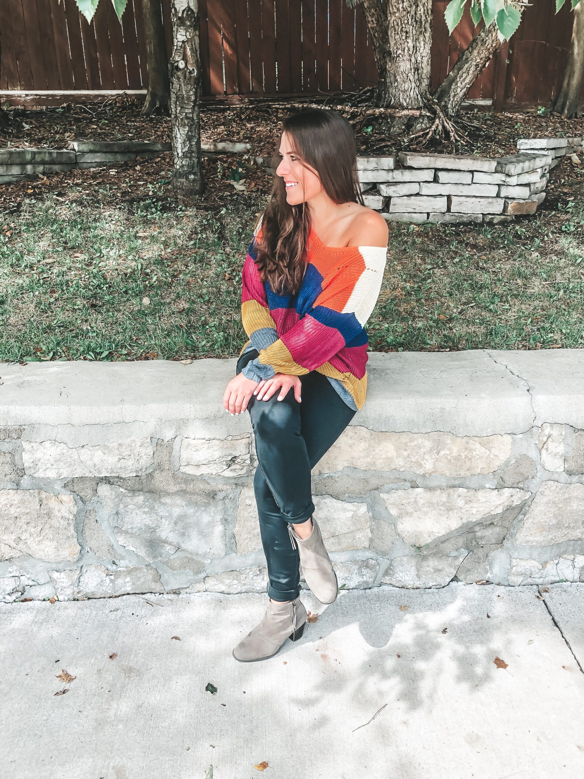 A woman wearing a colorful sweater sitting on a stone wall.
