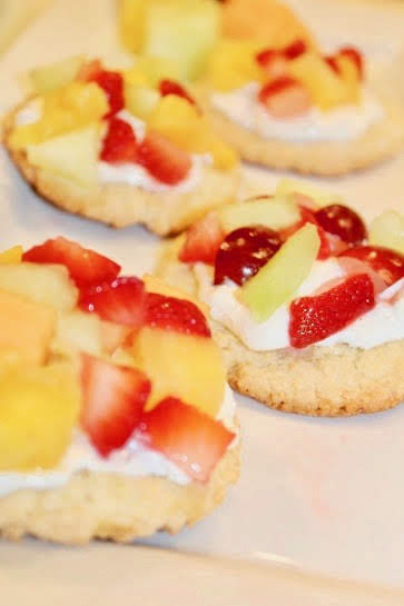A mini sugar cookie fruit pizza recipe topped with fruit and whipped cream.