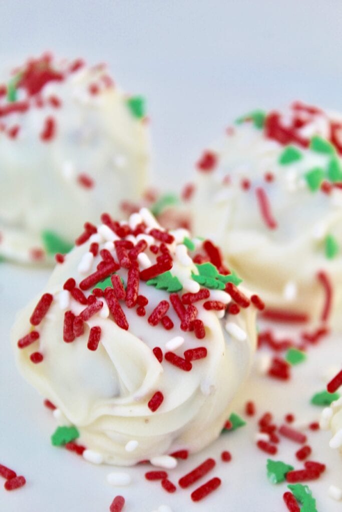 Christmas cookie truffles with white frosting and red and green sprinkles, made using a chocolate chip cookie dough.