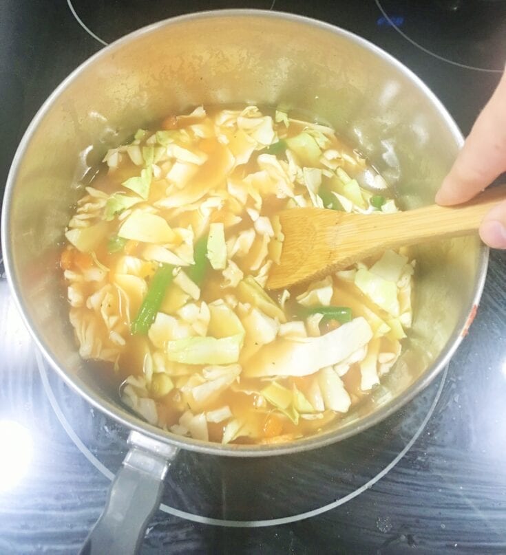 A person stirs a pot of Weight Watchers Cabbage Soup with a wooden spoon.