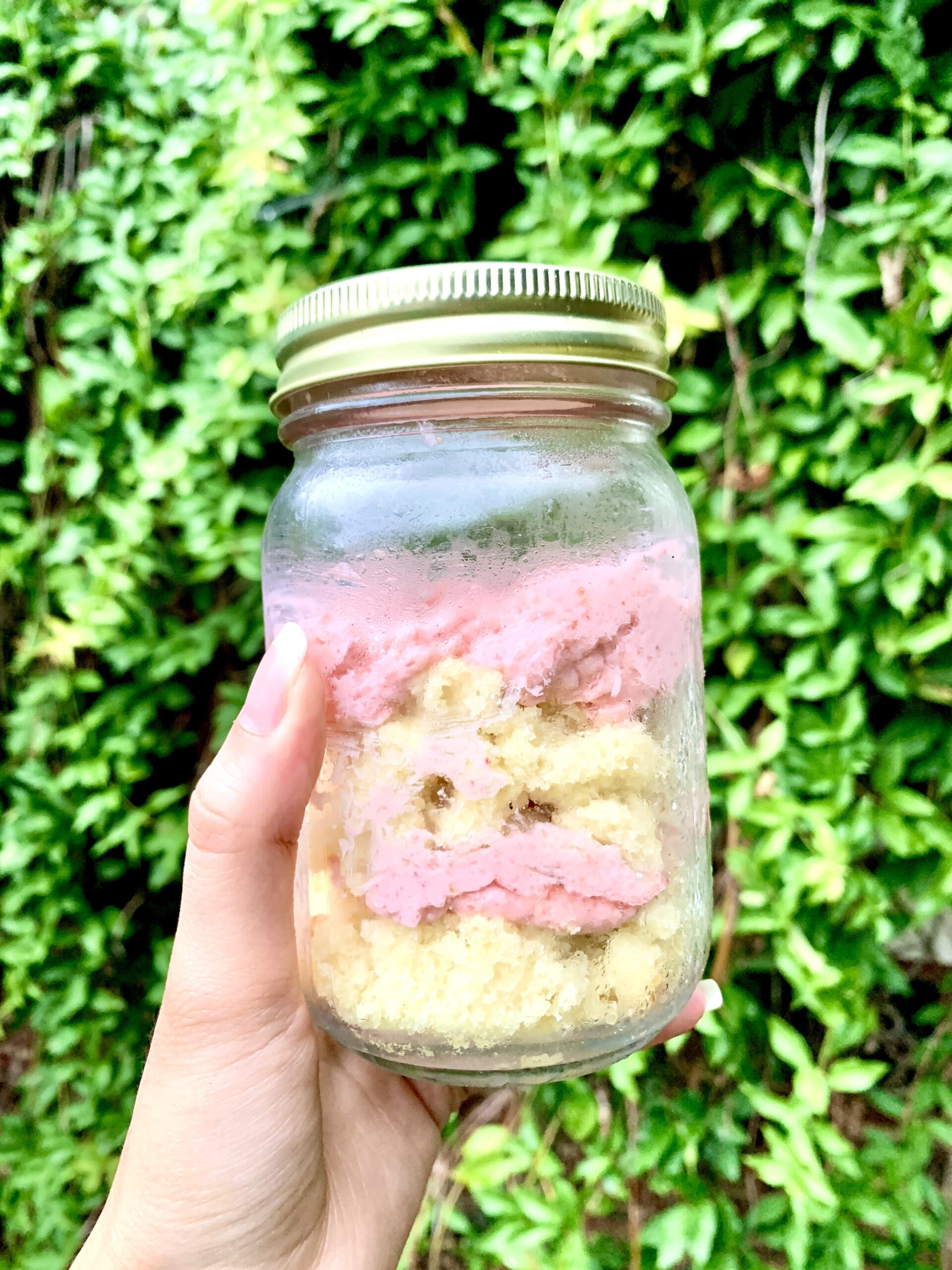 A person showcasing a delectable cake in a jar with pink frosting.