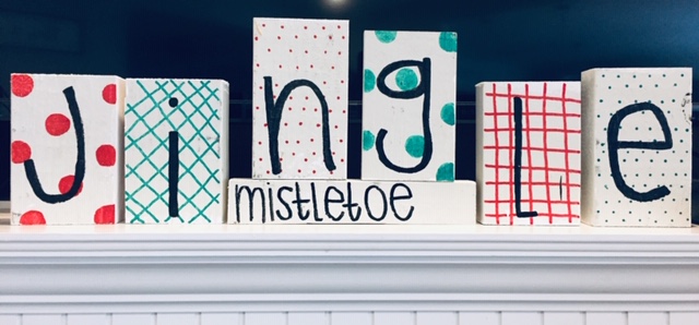 Blocks of wood decorated to spell out the word JINGLE with small block underneath reading MISTLETOE