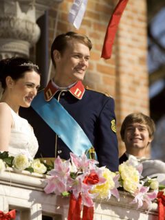 A man and woman in wedding dresses on a balcony in one of the best Hallmark royal Christmas movies.