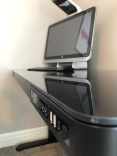 A black computer desk with a monitor on the Comhar All-in-One Standing Desk.