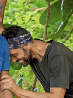 Two men, part of a Survivor duo, are sitting in a tree with a bandana on their heads.