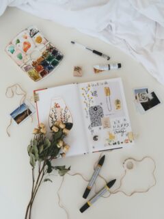 A bed adorned with a notebook, pens, and flowers, showcasing the best journals for art journaling.
