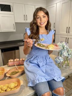 A woman in a blue apron showcasing Hannah Ann's Kitchen Essentials with a plate of food.