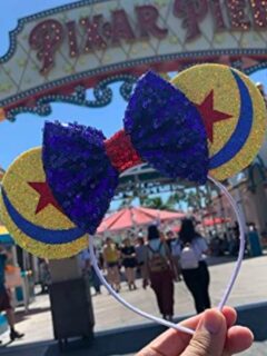 A person is holding a Mickey Mouse headband in front of Disneyland.