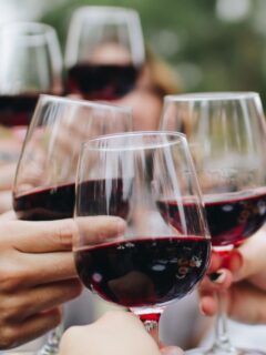 Individuals toasting red wine glasses.