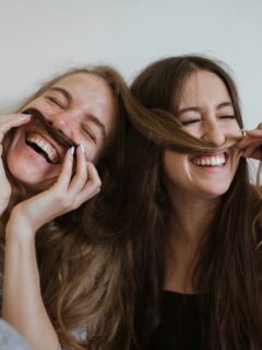Two young women laughing with their mustaches, showcasing a vibrant Capricorn and Virgo friendship