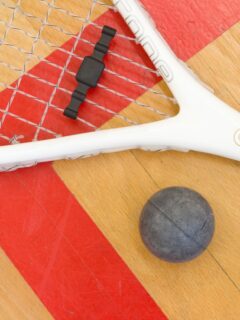 A squash racket and ball on a wooden floor, showcasing the best shoes for racquetball.