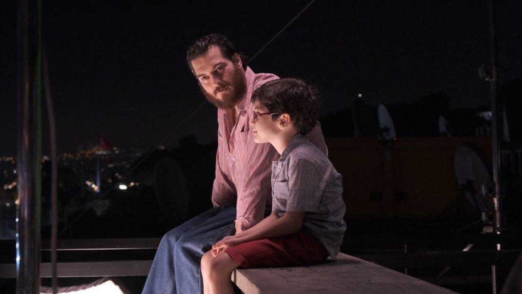 Mehmet and Ali sit on top of a building together and talk about mothers. 