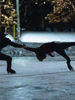 Two people, Kat Baker and her partner, spinning out quotes while gracefully skating on an ice rink at night.