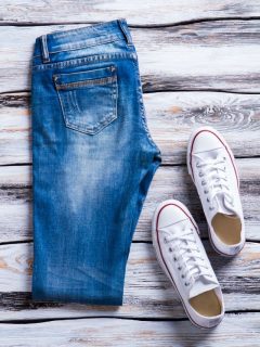 A pair of jeans and sneakers on a wooden background, showcasing how to wear skinny jeans with tennis shoes.