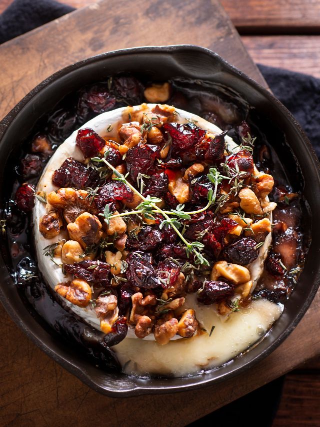 baked brie in cast iron skillet with dried cranberries, chopped awlnuts, maple syrup, and thyme