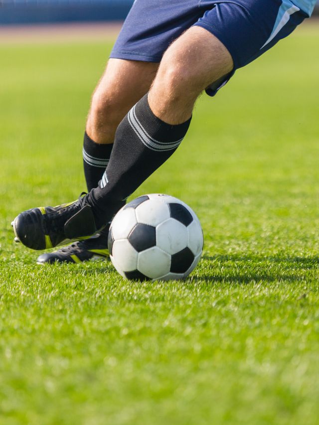 black shoe legs kicking soccer ball