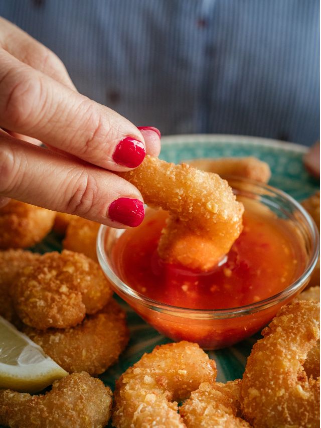 hand dipping breaded shrimp in chili sauce