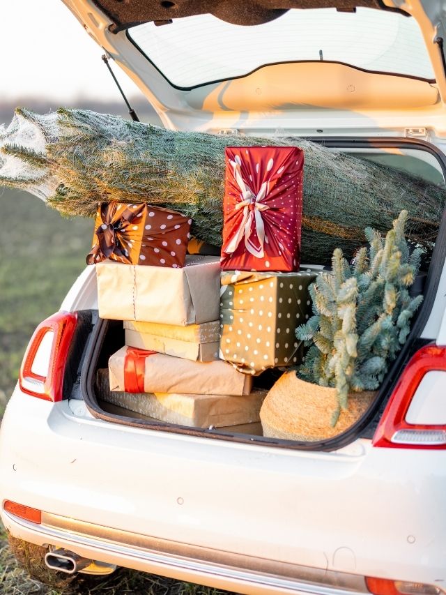 car trunk full of gift boxes and Christmas tree on the field at sunset