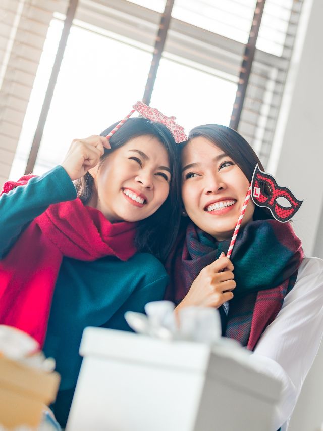 happy two women best friends wearing scarf playing with paper props having fun together during new year