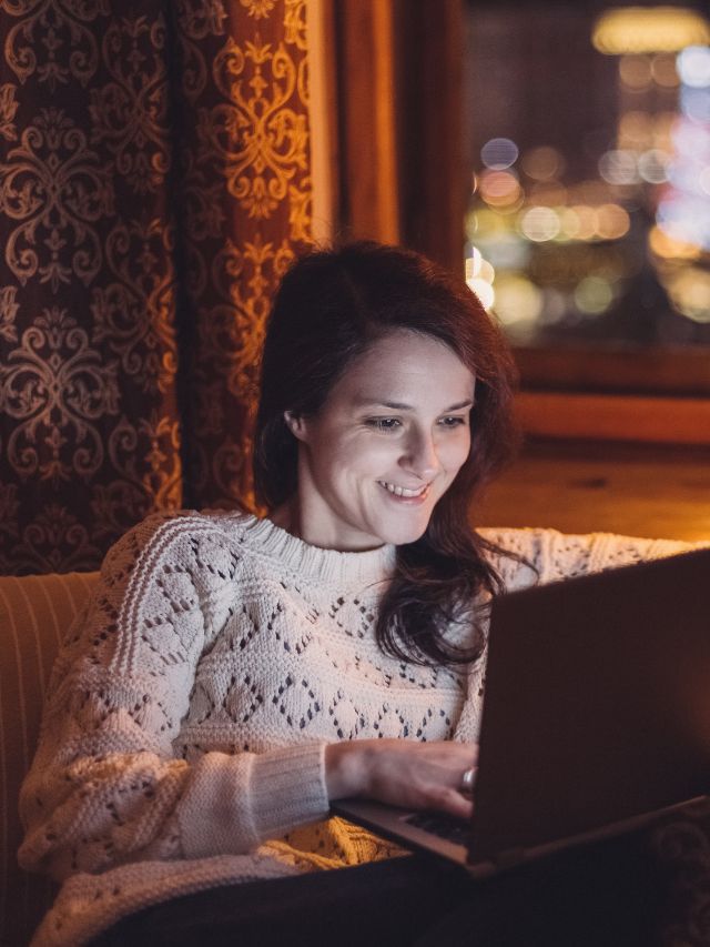 woman in sweater smiling at laptop