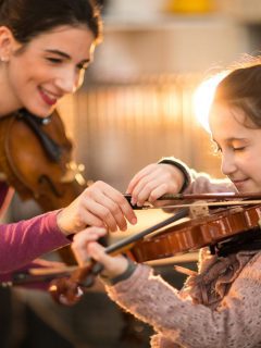 woman teaching girl how to play violin