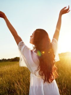 A woman is standing in a field with her arms outstretched, embodying a sense of divine connection.