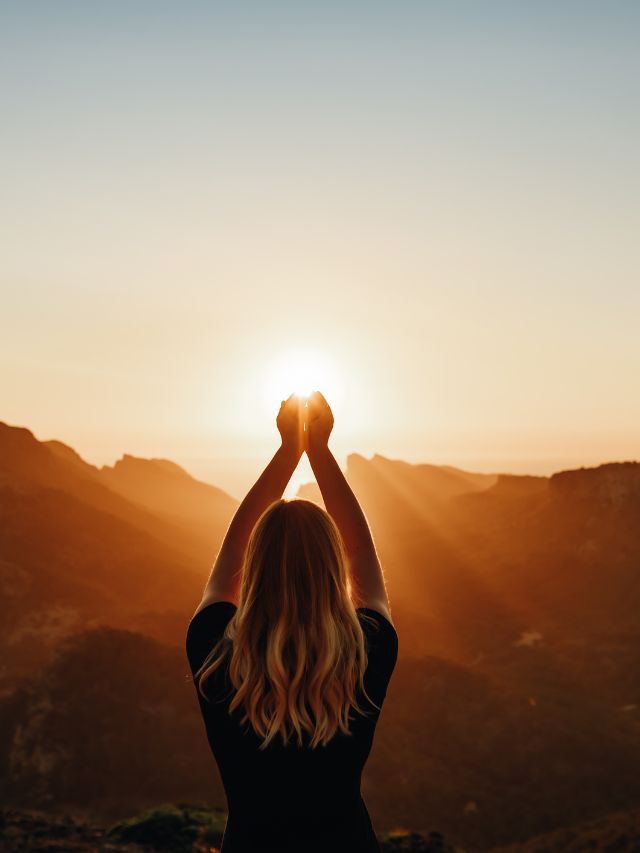 young woman in spiritual pose holding the light in front of mountains