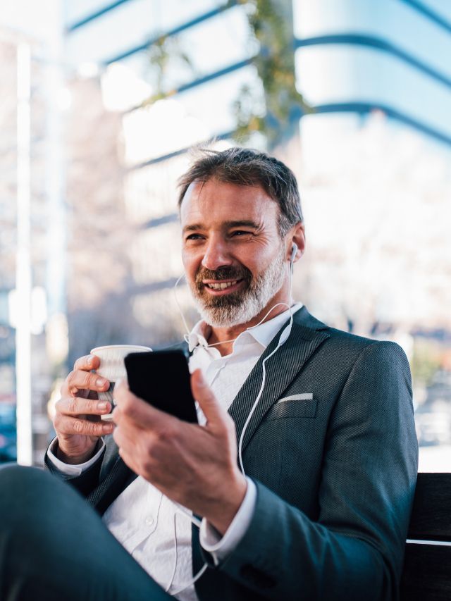 man sitting outside drinking coffee and holding phone