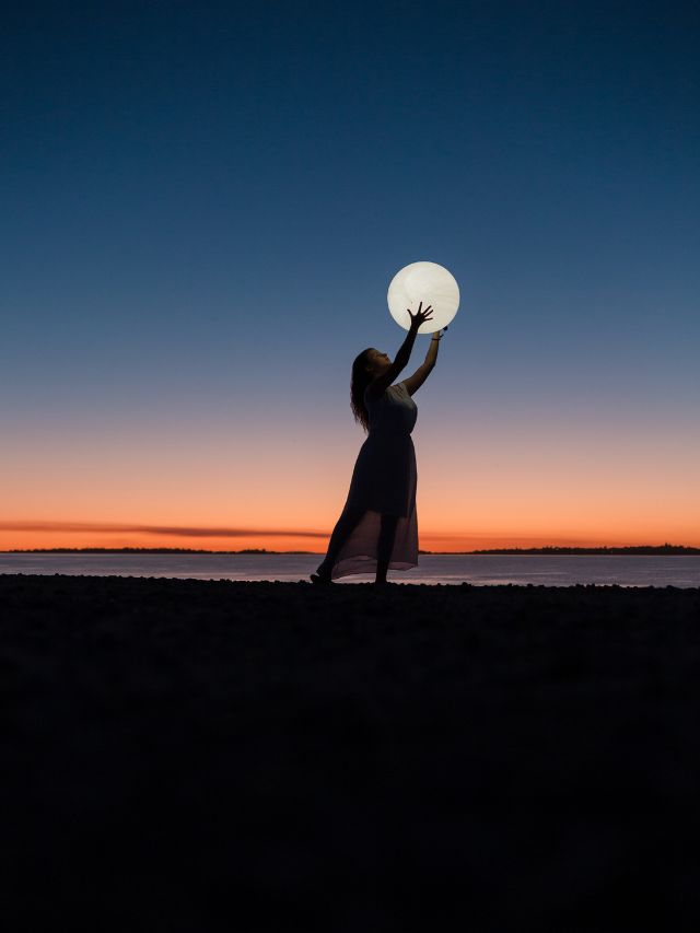 girl holding moon up in air at sunset