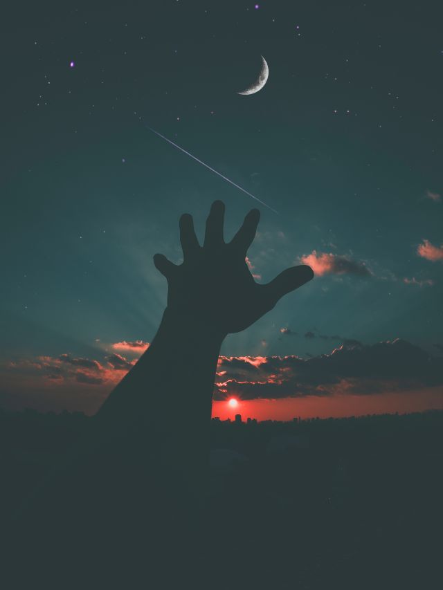 hand reaching in the sky for the moon during sunset