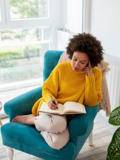 A woman is practicing the 55x5 manifestation method by sitting in a chair and reading a book.