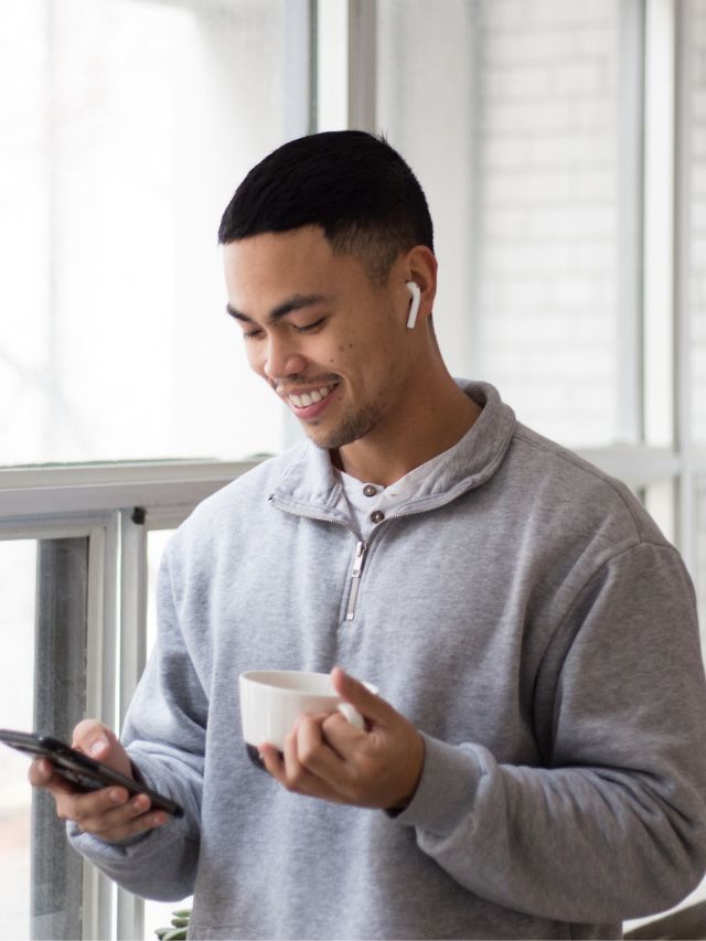 man smiling at phone while holding coffee