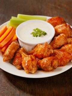 A plate with chicken wings, carrots, celery and dip.