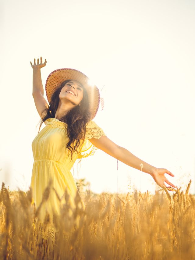 happy young woman with open arms in the wheat field on a sunny day
