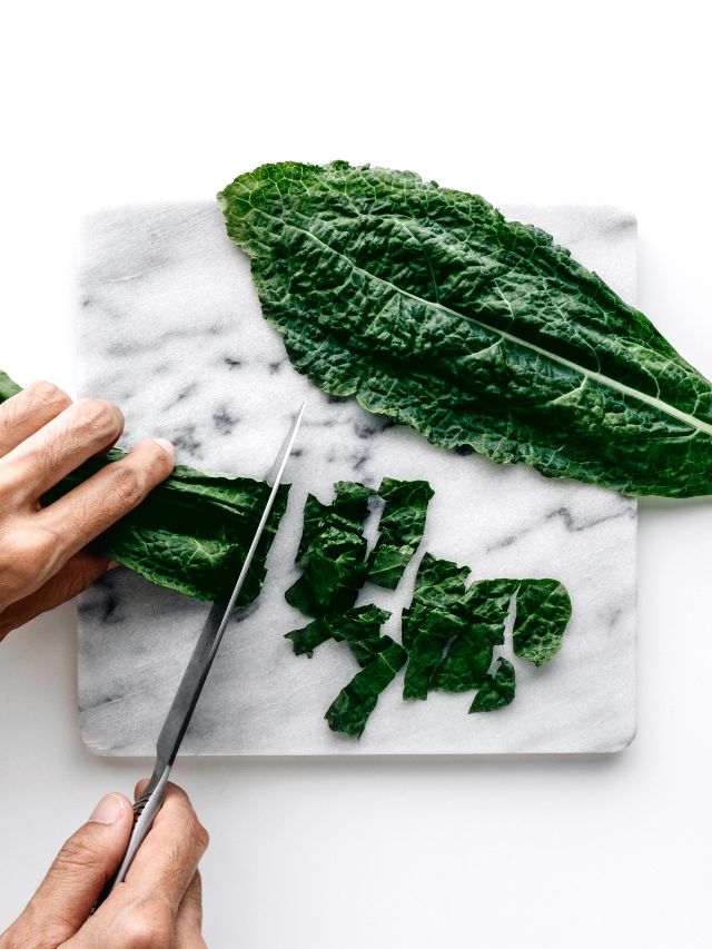 hands cutting organic green kale leaves on marble cutting board