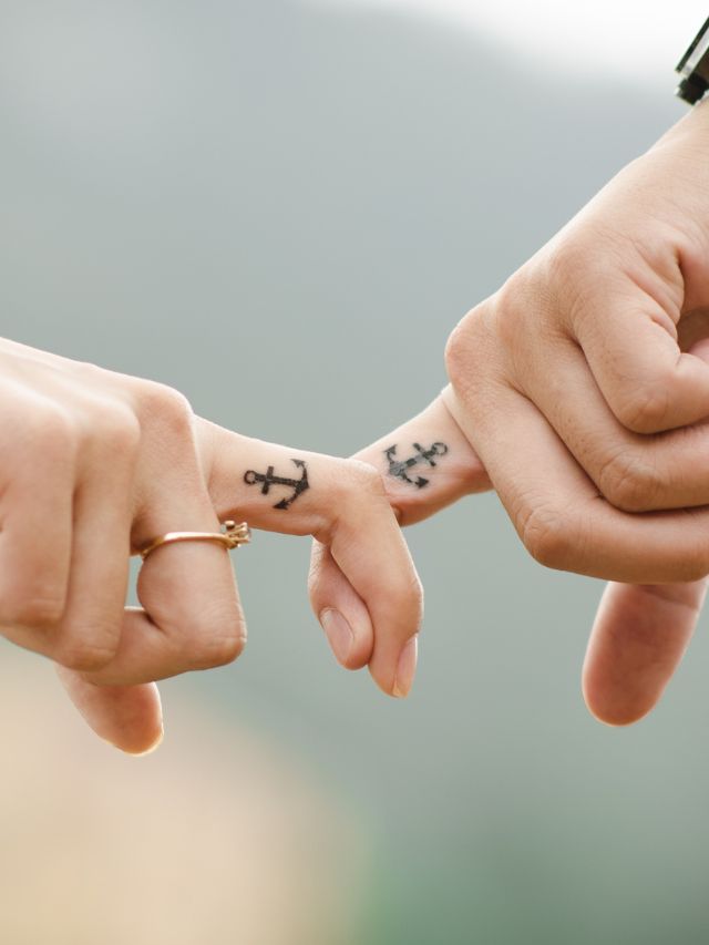 man and woman interlocking fingers with anchor tattoo
