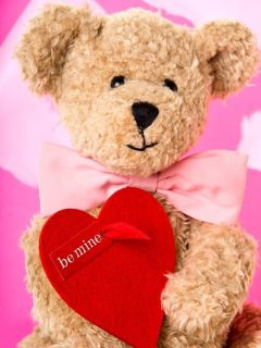 A valentine's day gift teddy bear holding a red heart on a pink background.