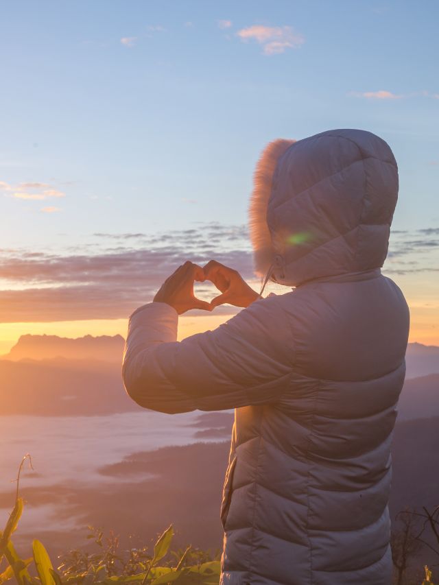 woman making heart shape with hands in front of sunrise