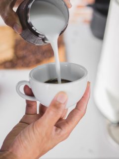     Description: A person pouring milk into a cup of coffee with cream.