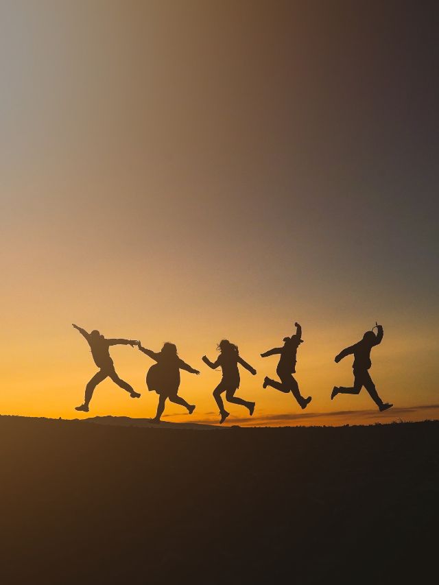 group of friends jumping in front of sunset
