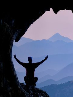 A man practicing quantum jumping manifestation in a cave with his arms outstretched.