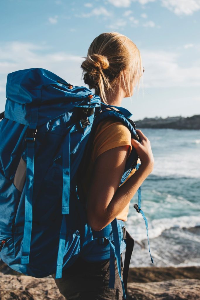 woman carrying large blue backpack looking at the ocean