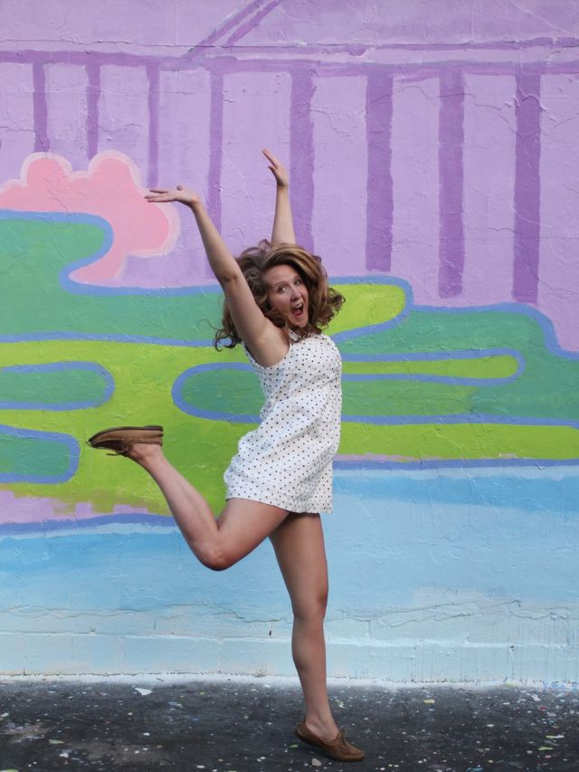 woman in white midi dress jumping with arms in the air
