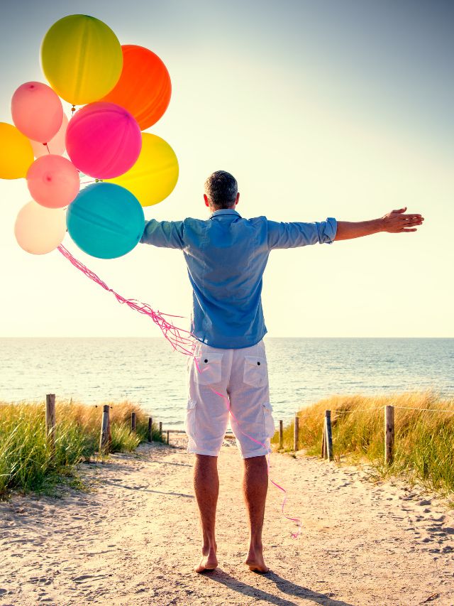 happy male on the beach holding balloons